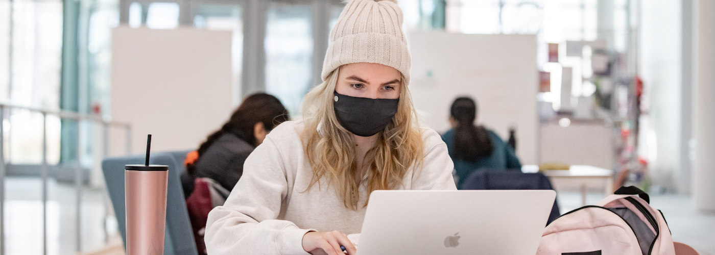 girl wearing hat and mask using laptop